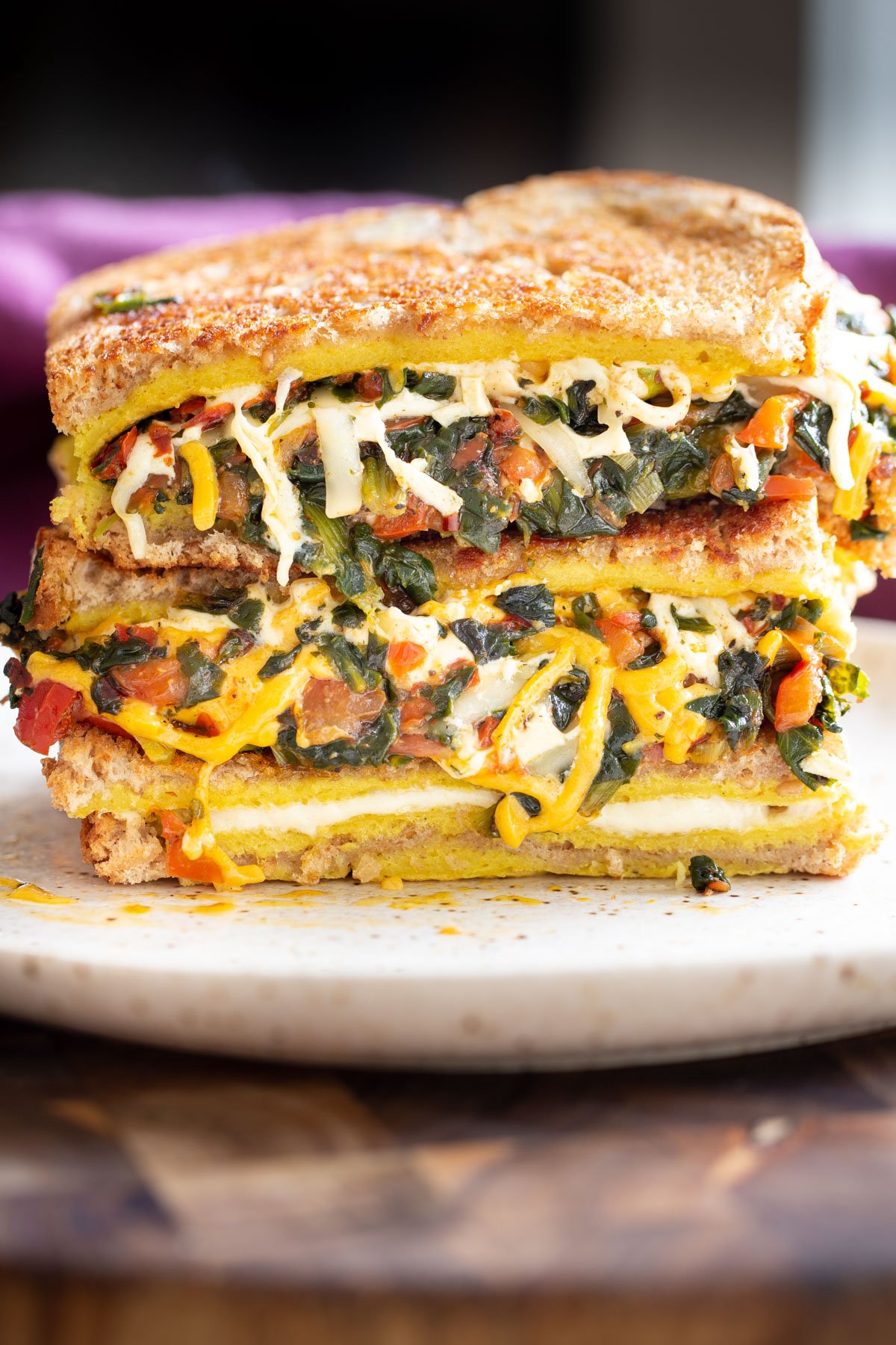 a stacked moong egg sandwich filed with spinach and cheese as well as vegetables