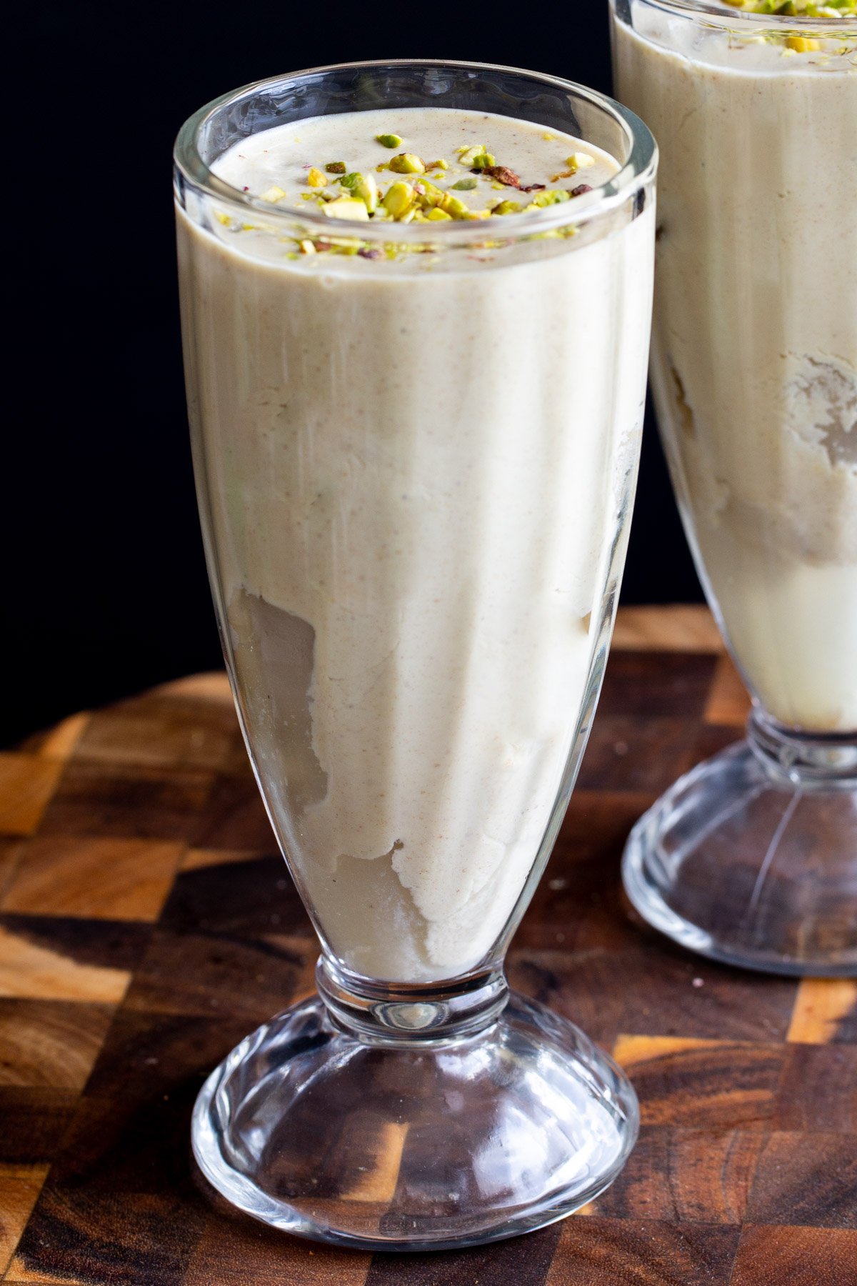 side shot of a glass with Indian pistachio lassi sprinkled with pistachios