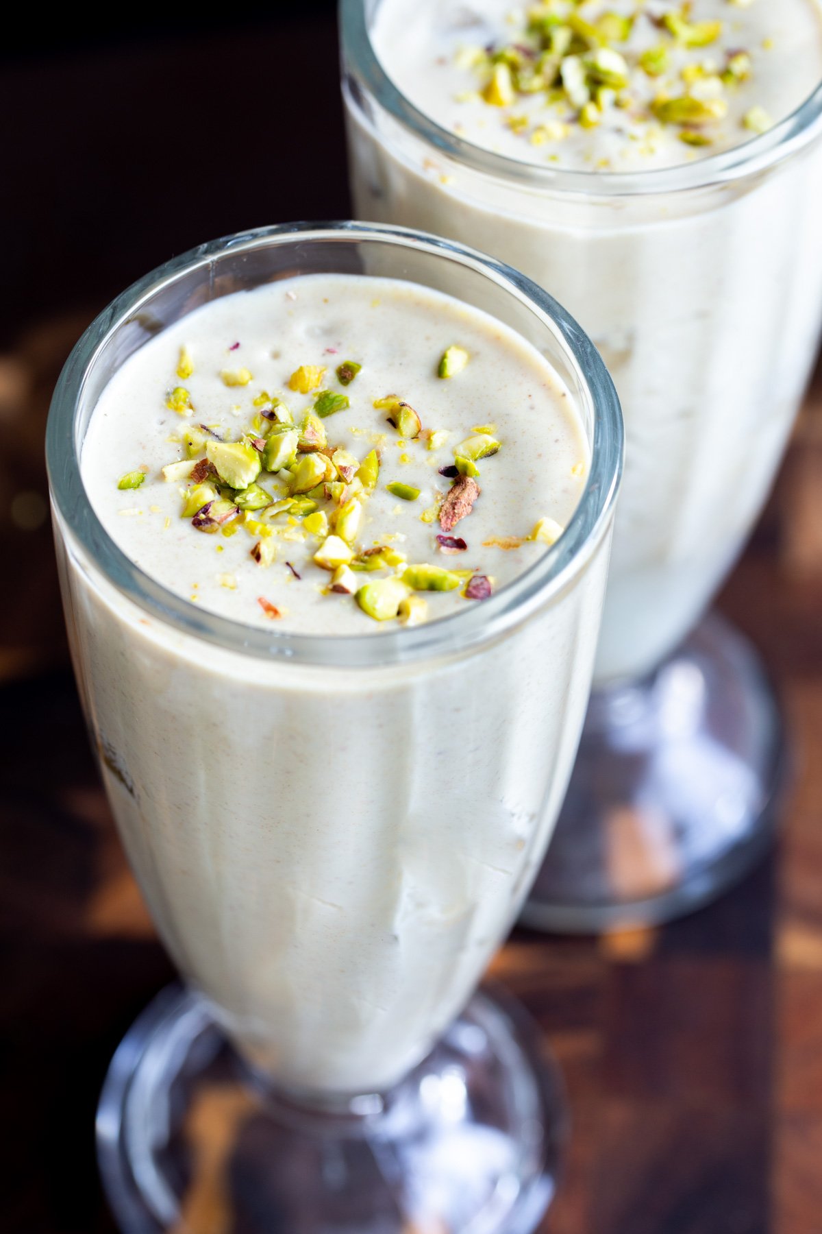 two milkshake glasses with Indian baklava flavored lassi sprinkled with pistachips