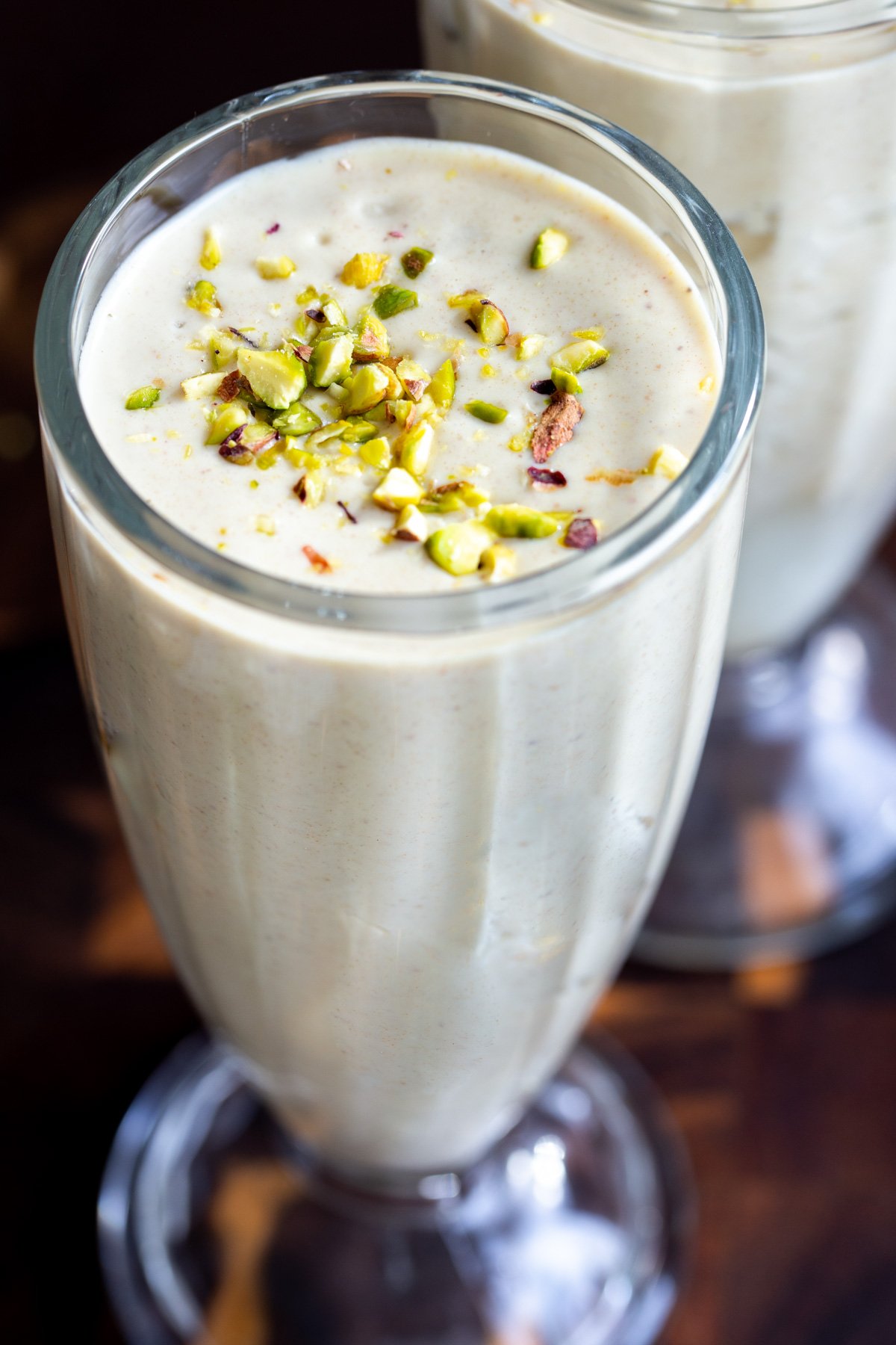 a tall glass with Indian Baklava Lassi sprinkled with pistachios