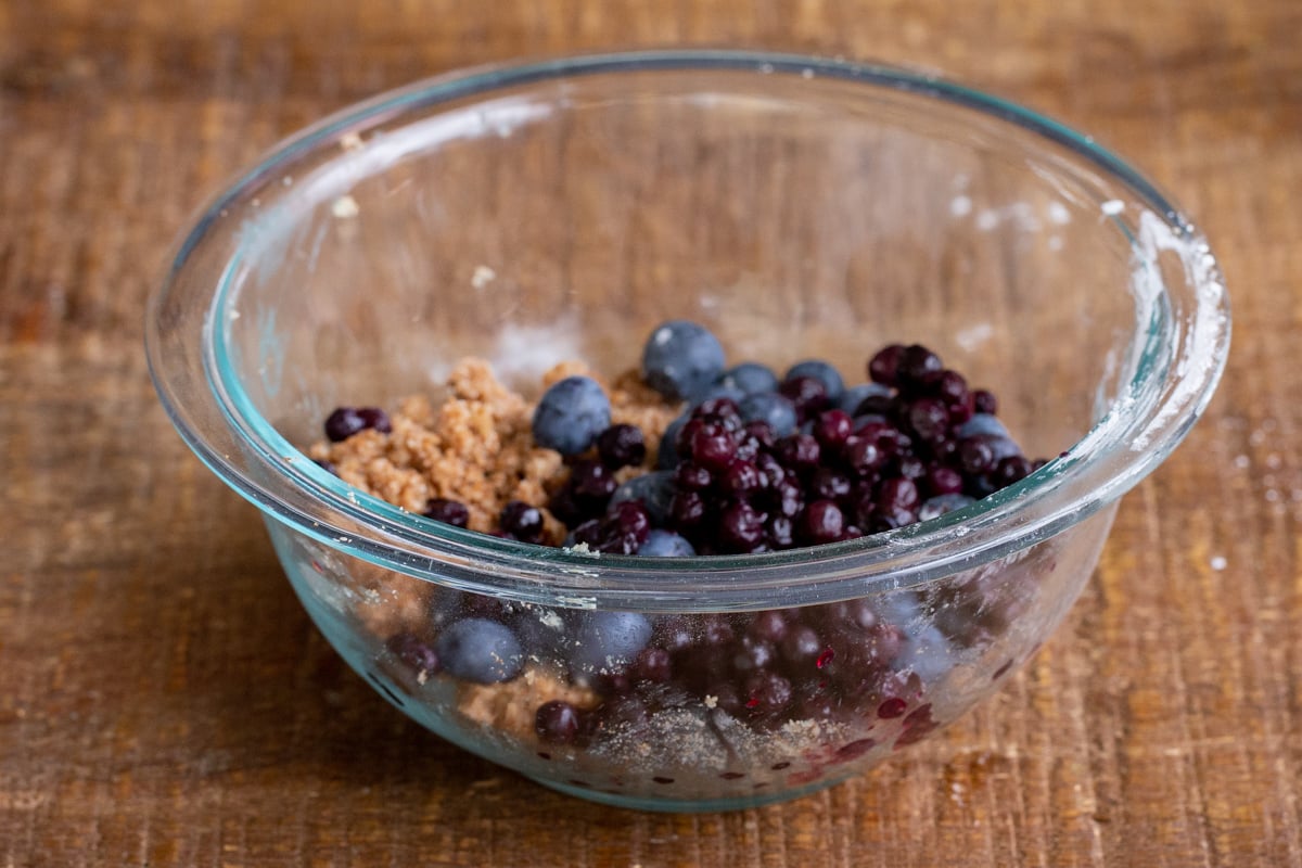 fresh and frozen blueberries being added to streusel dough