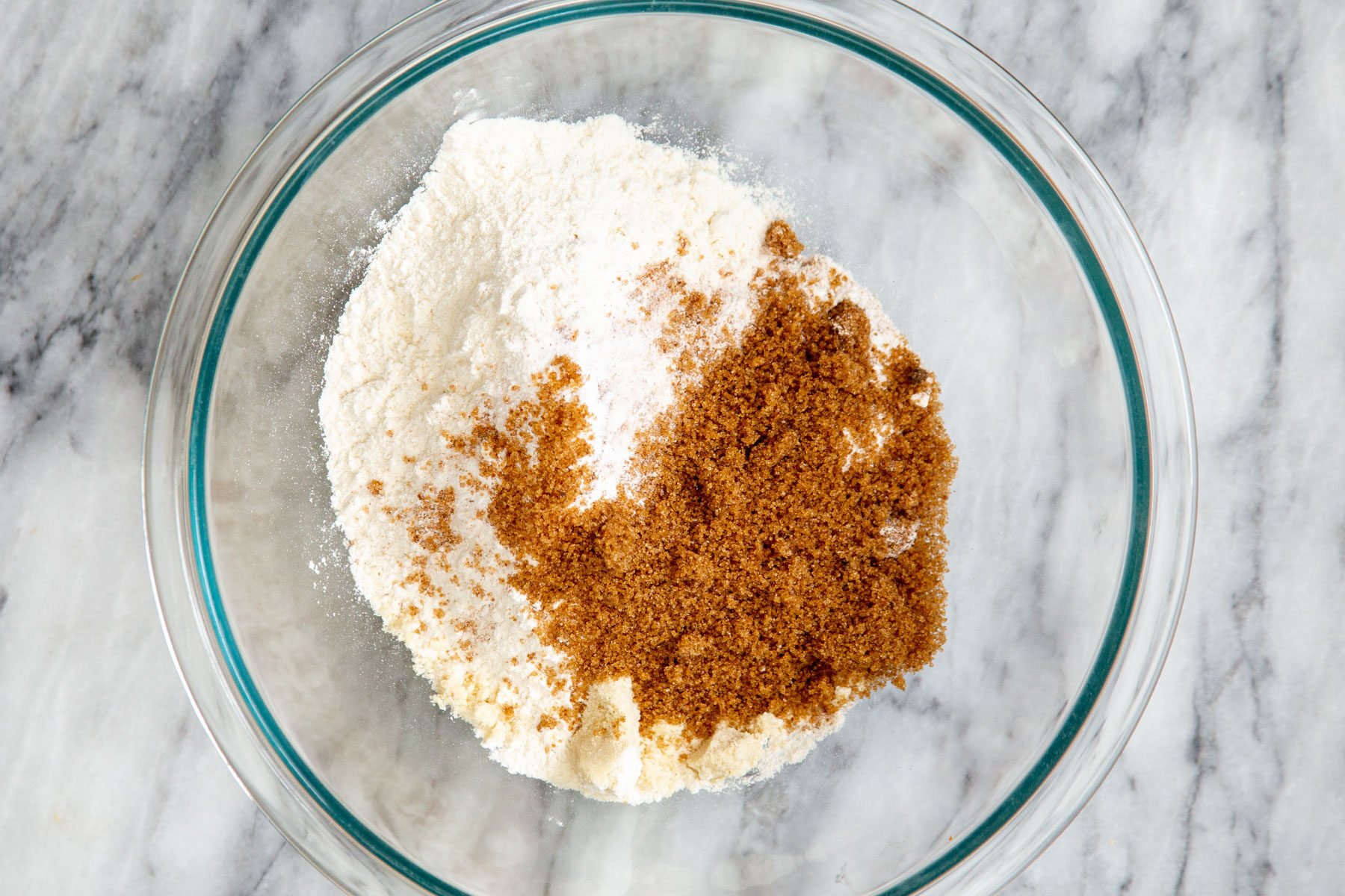 sugar being added to dry ingredients in a glass bowl
