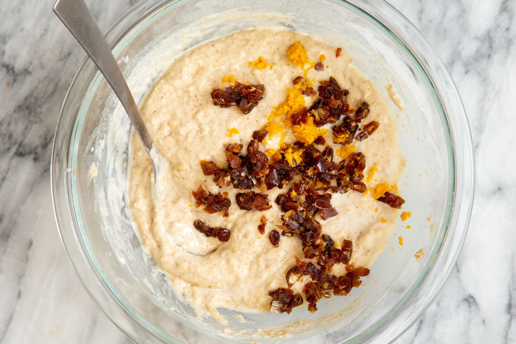 chopped dates and orange zest being added to carrot cake batter