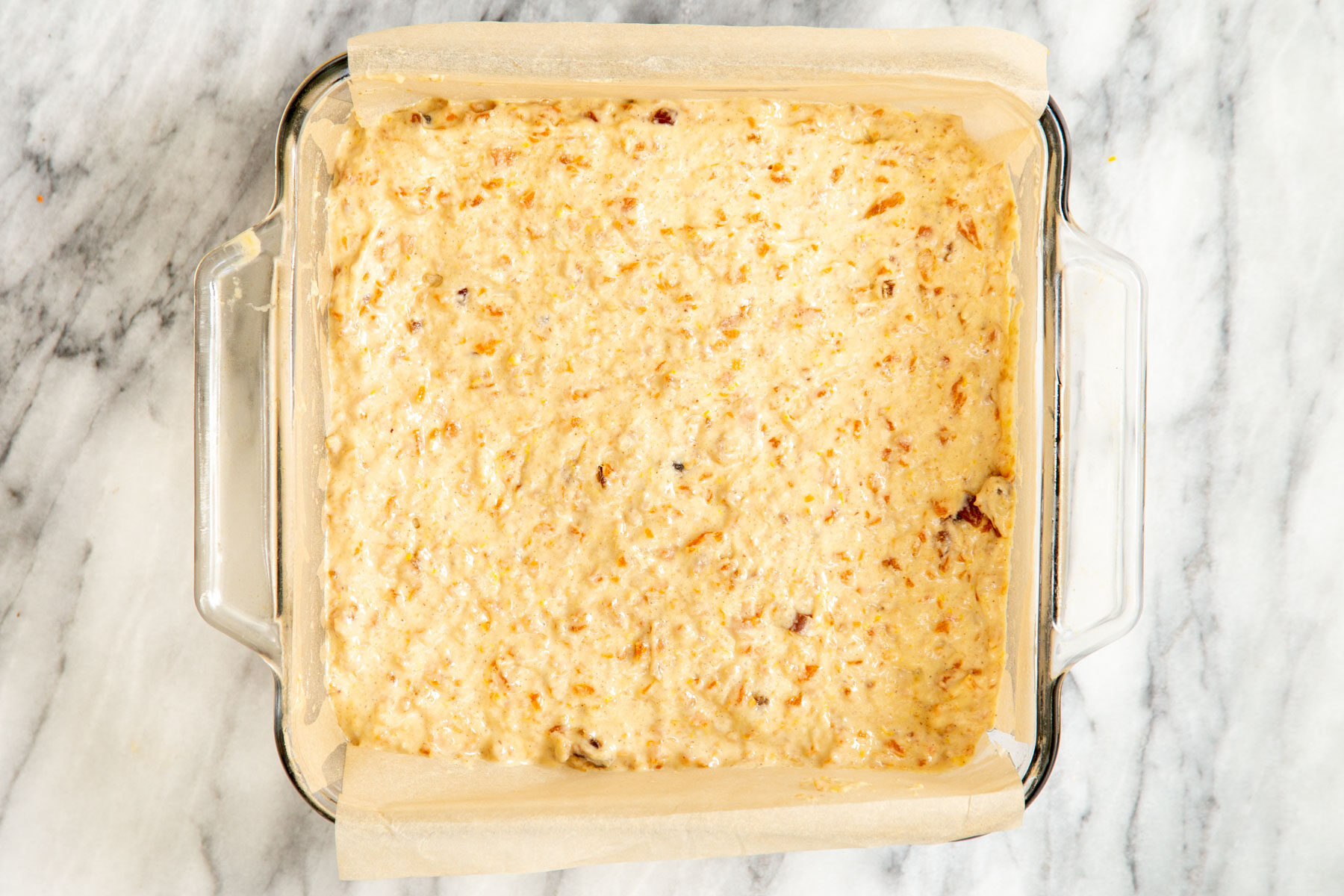 carrot cake bars batter being spread into a square glass pyrex dish