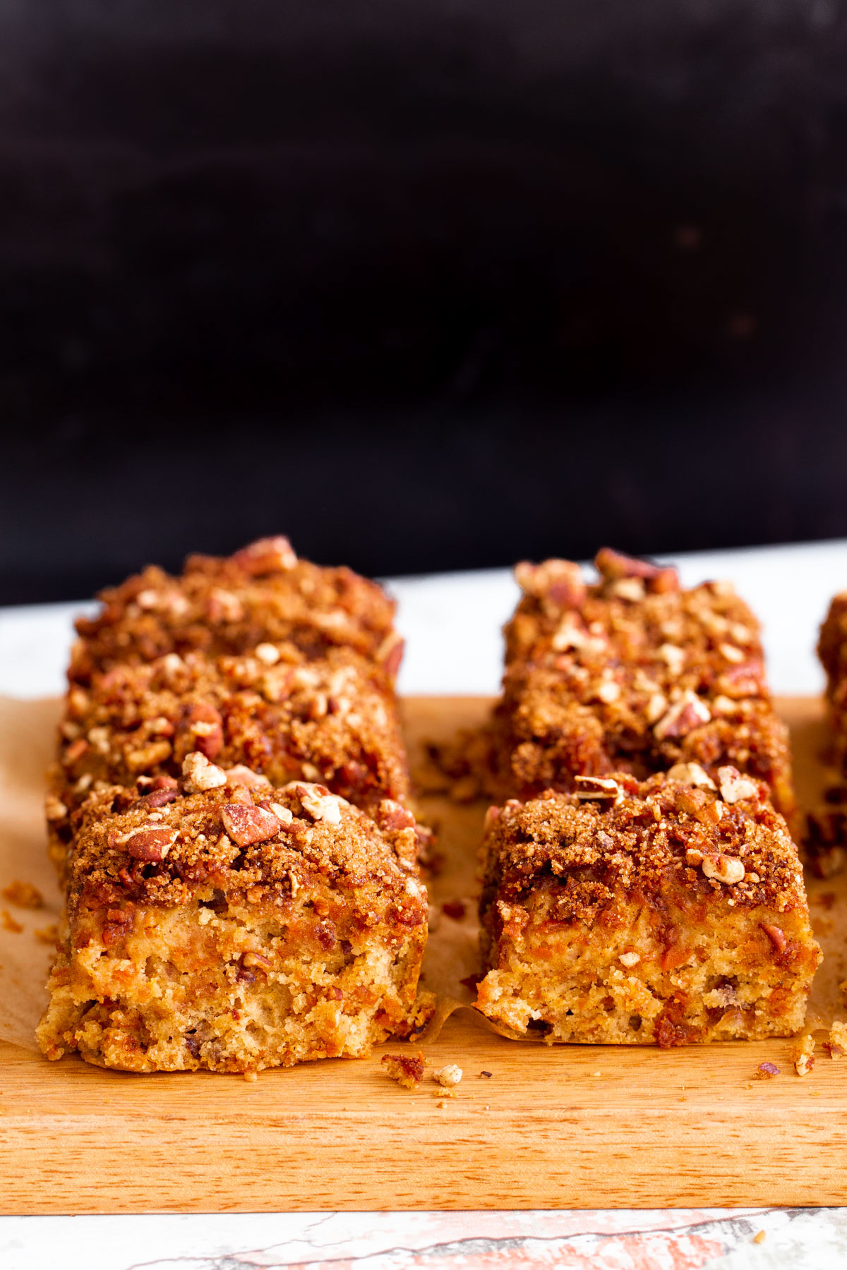 vegan carrot cake bars on a wooden board against a black background