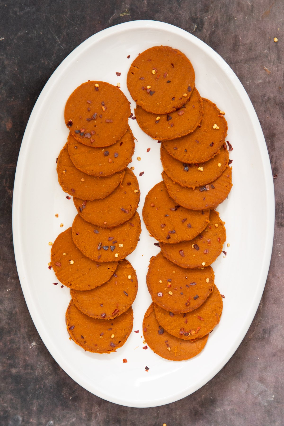 sliced glutenfree vegan pepperoni on a white plate sprinkled with red pepper flakes