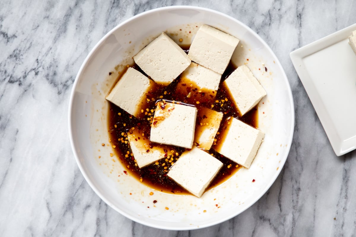 sliced tofu being added to a bowl with marinade