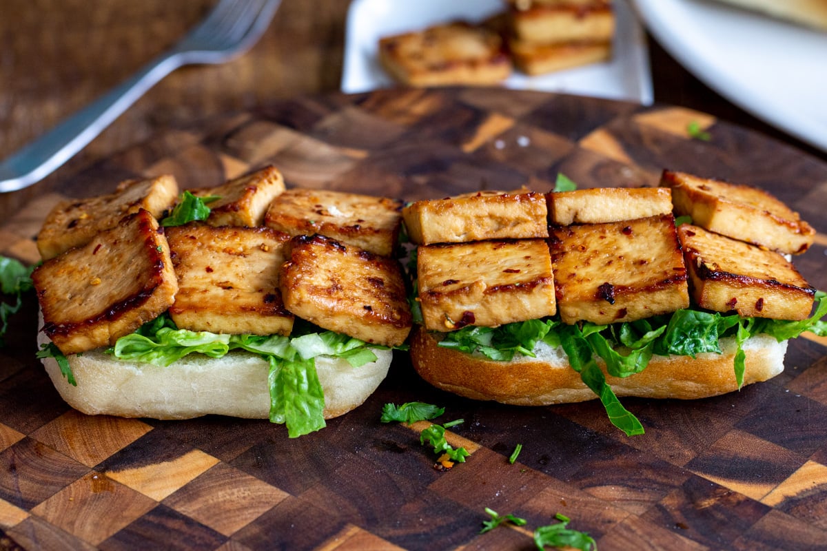 a sandwich being assembled with lettuce and baked chili garlic tofu