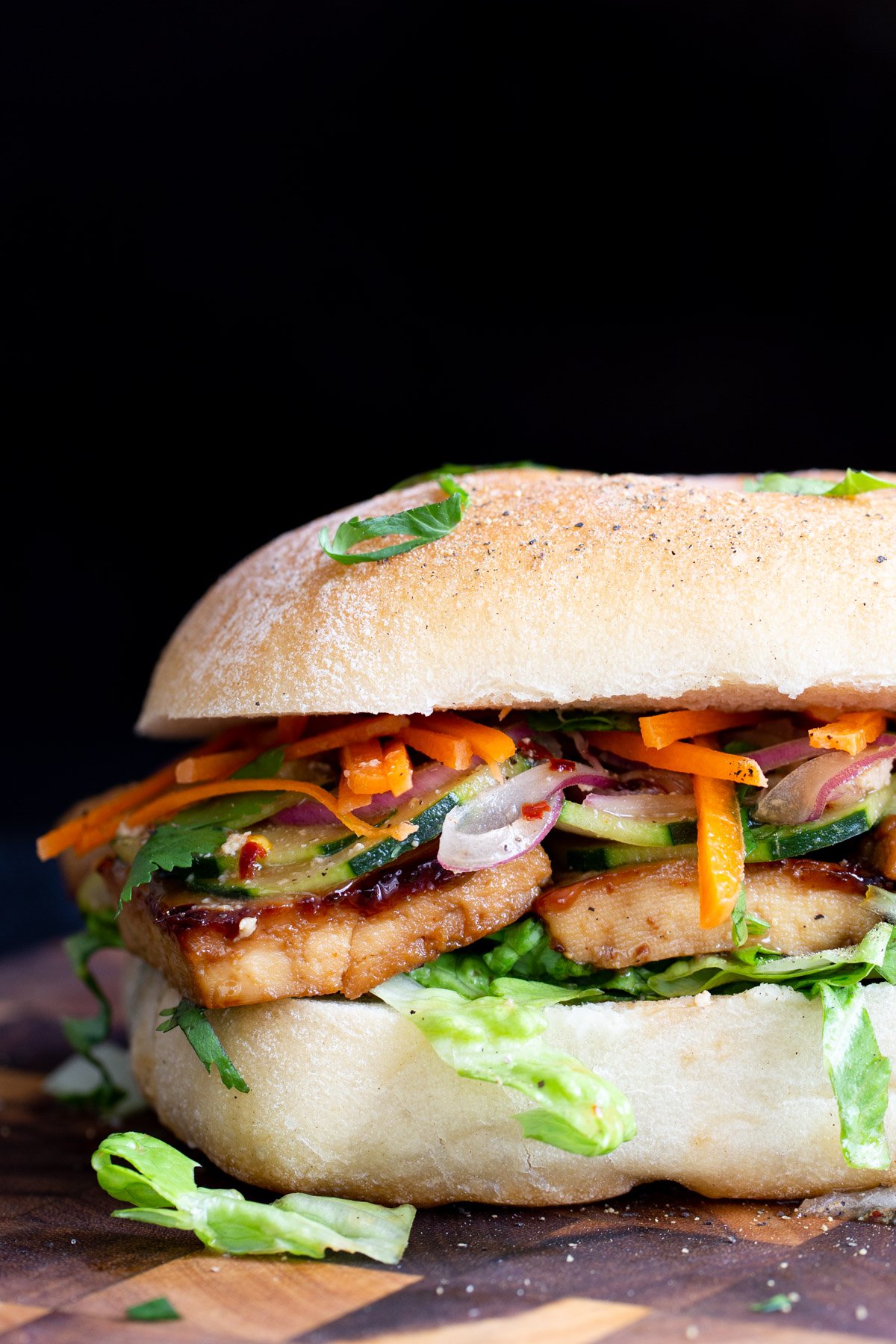 a vegan chili garlic tofu sandwich on a wooden chopping board being sliced in the middle