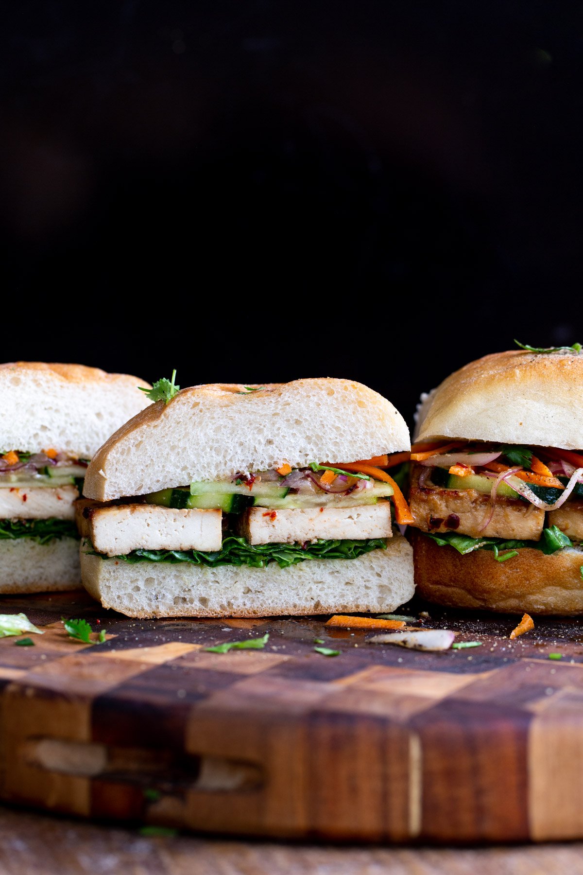 sliced vegan tofu sandwiches with chopped veggies on a wooden board