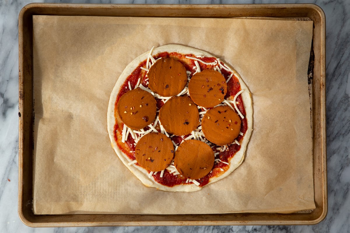 almond flour pizza crust being topped with pepperoni and vegan cheese