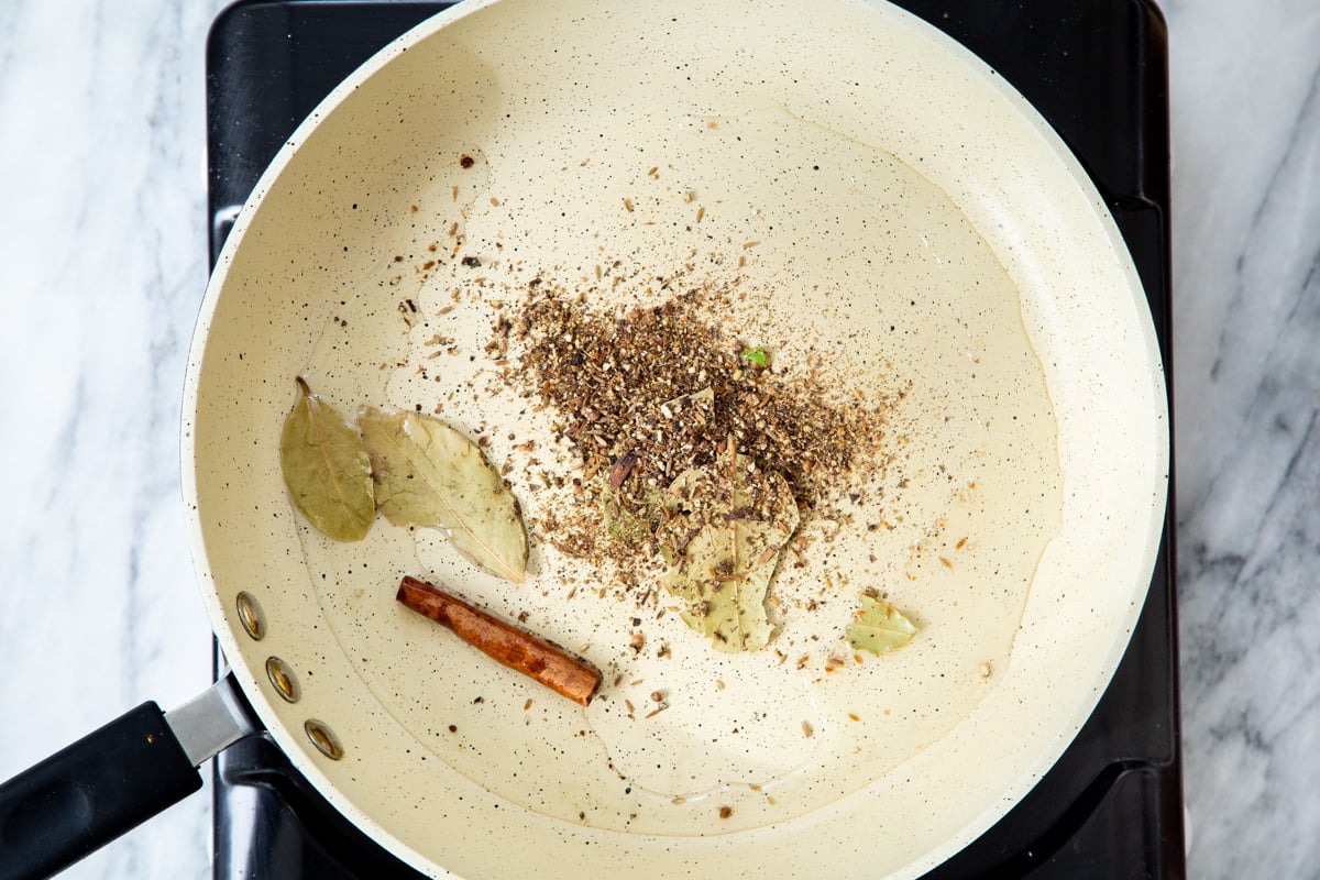 a frying pan with hot oil with added whole spices for making tempering