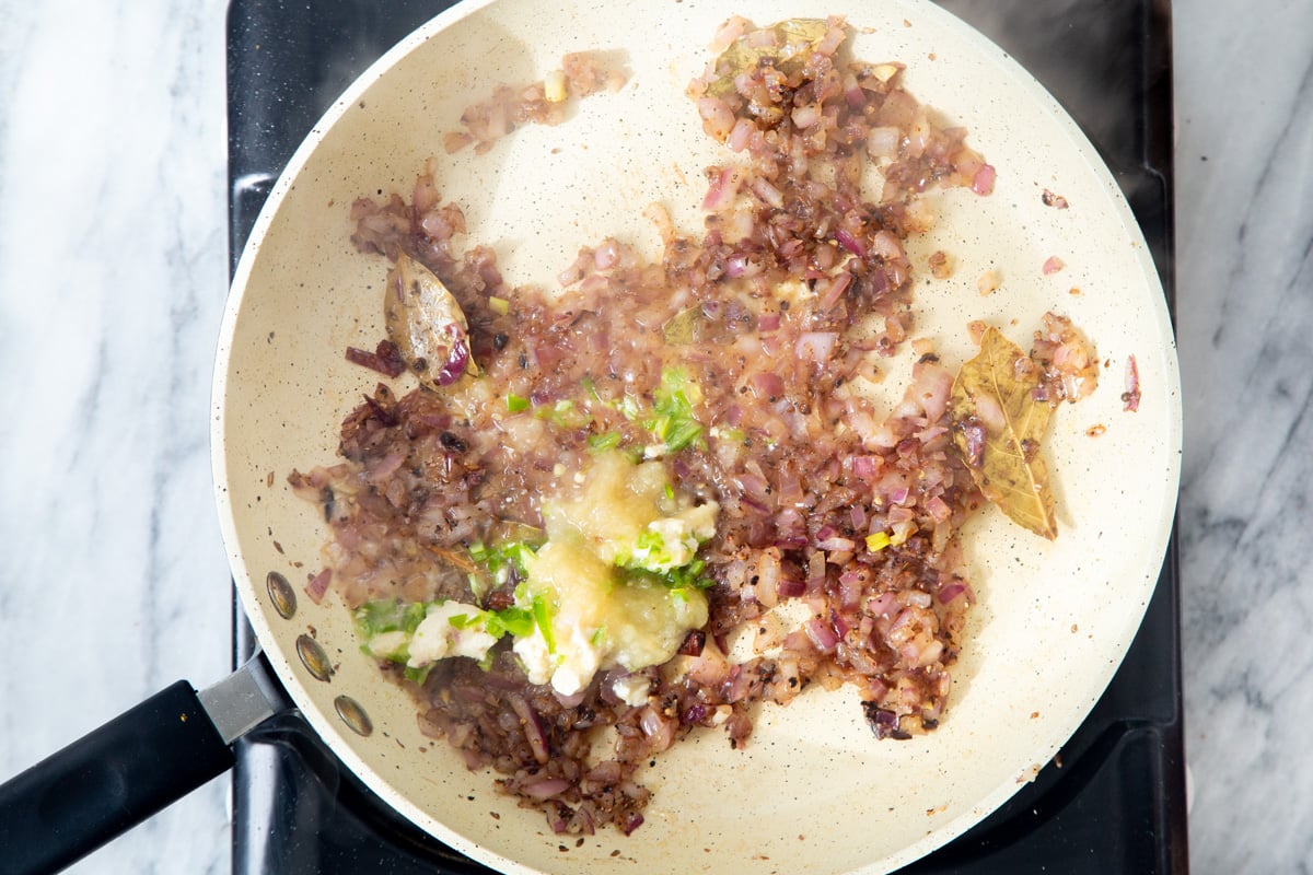 ginger garlic paste being added to sauteed onion and Indian tempering in a frying pan