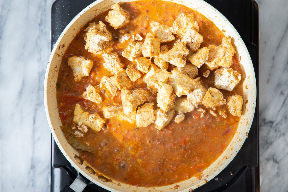 baked tofu chunks being added to a frying pan with Indian gravy