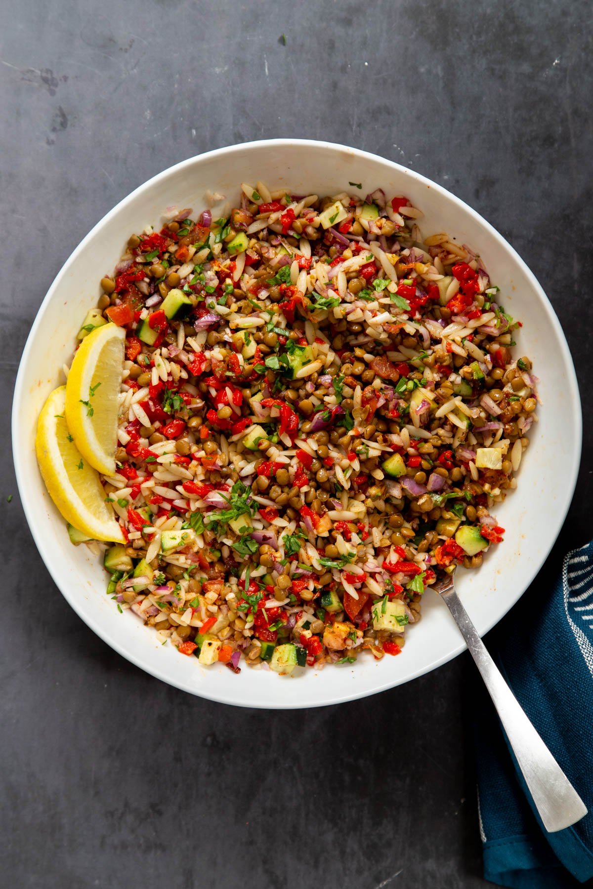 a bowl if vegan farro and lentil salad with vegetables and lemon olive oil dressing in a white salad bowl