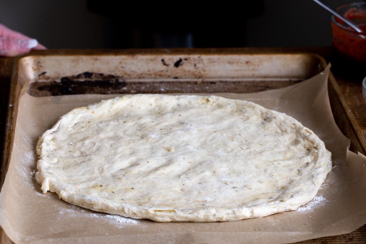 vegan pizza dough being shaped into a circle on a baking sheet