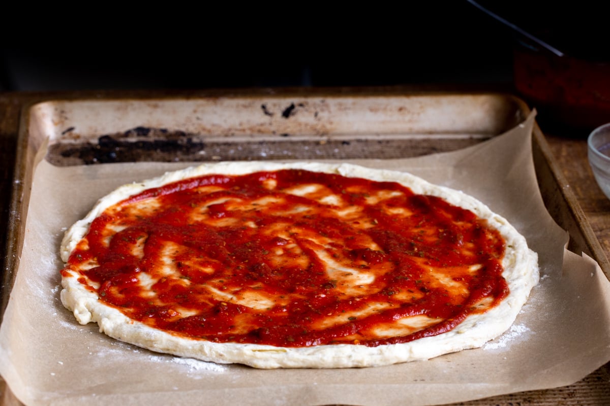 marinara sauce being spread on vegan pizza dough