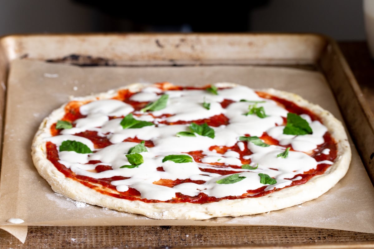 vegan liquid mozzarella cheese being spread over marinara sauce to make pizza