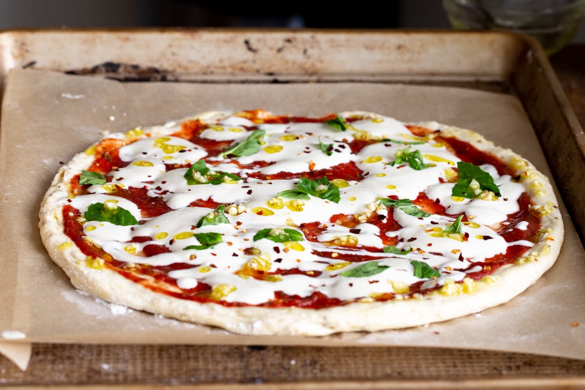 garlic oil and red pepper flaked being sprinkled over vegan mozzarella pizza on a baking sheet