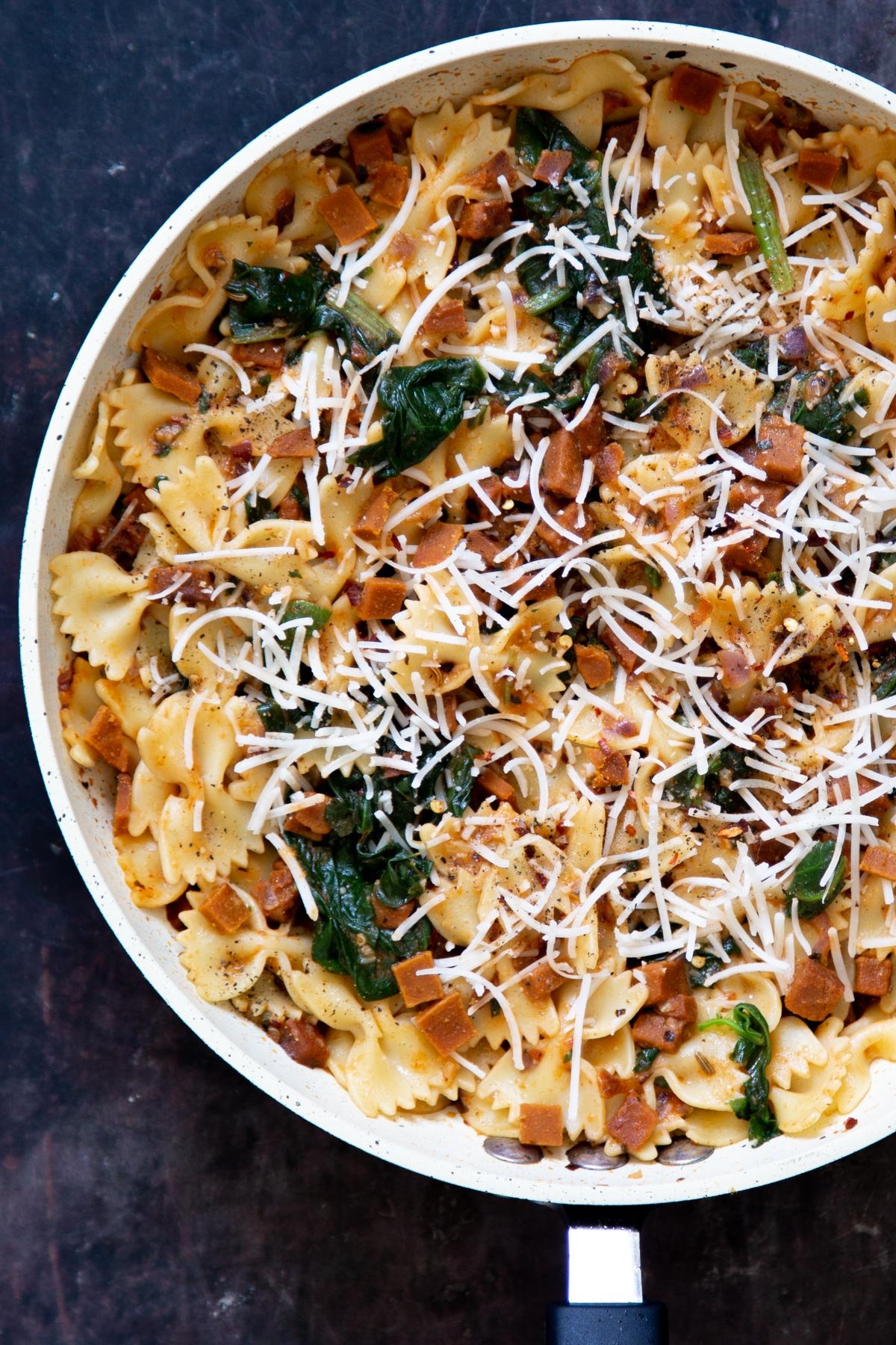 overhead shot of a pan with vegan pepperoni pasta sprinkled with vegan parmesan cheese
