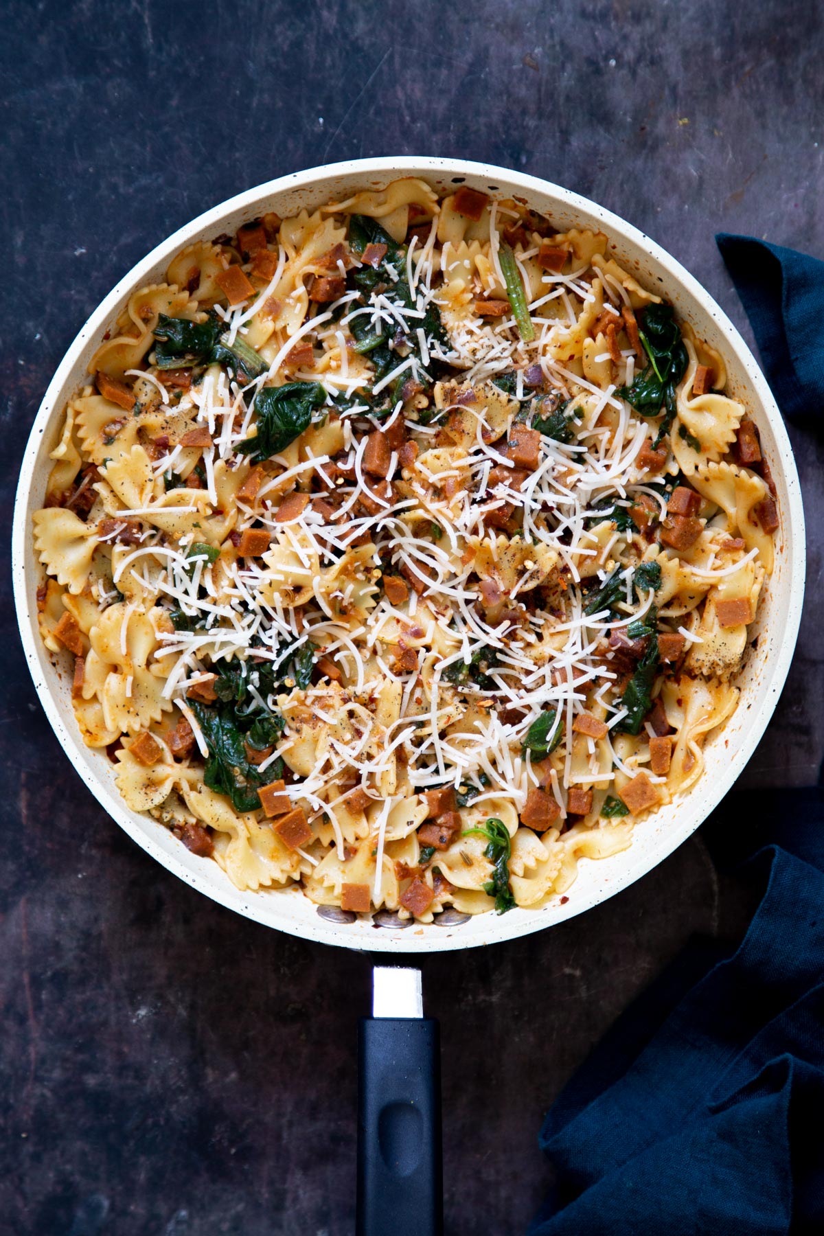 a pan with pasta tossed with spinach, vegan sausage and cheese