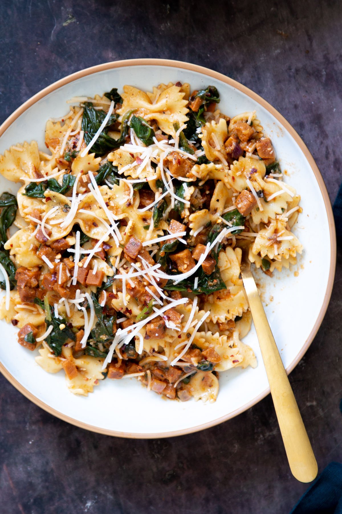 a plate with vegan pepperoni pasta with spinach and vegan parmesan with a golden fork on the side