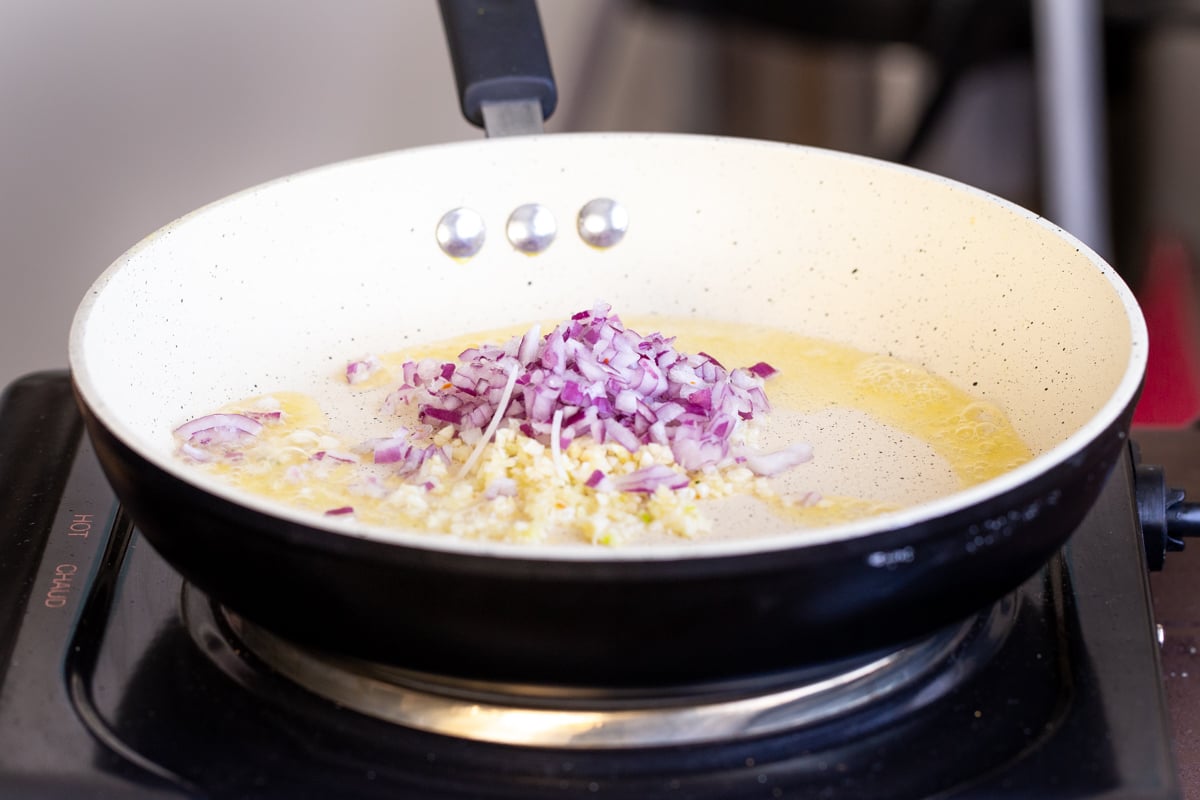 chopped onions and minced garlic being added to a sauteeing pan
