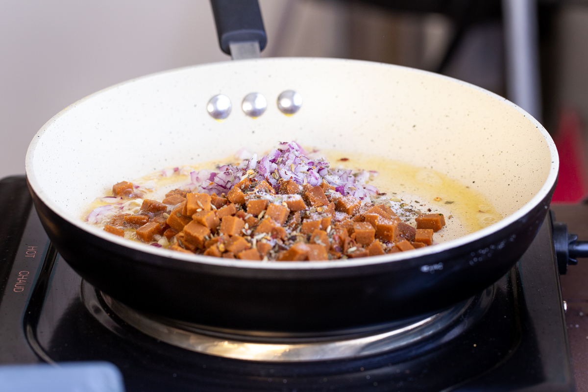 vegan pepperoni and minced onion being added to a frying pan to make pasta sauce