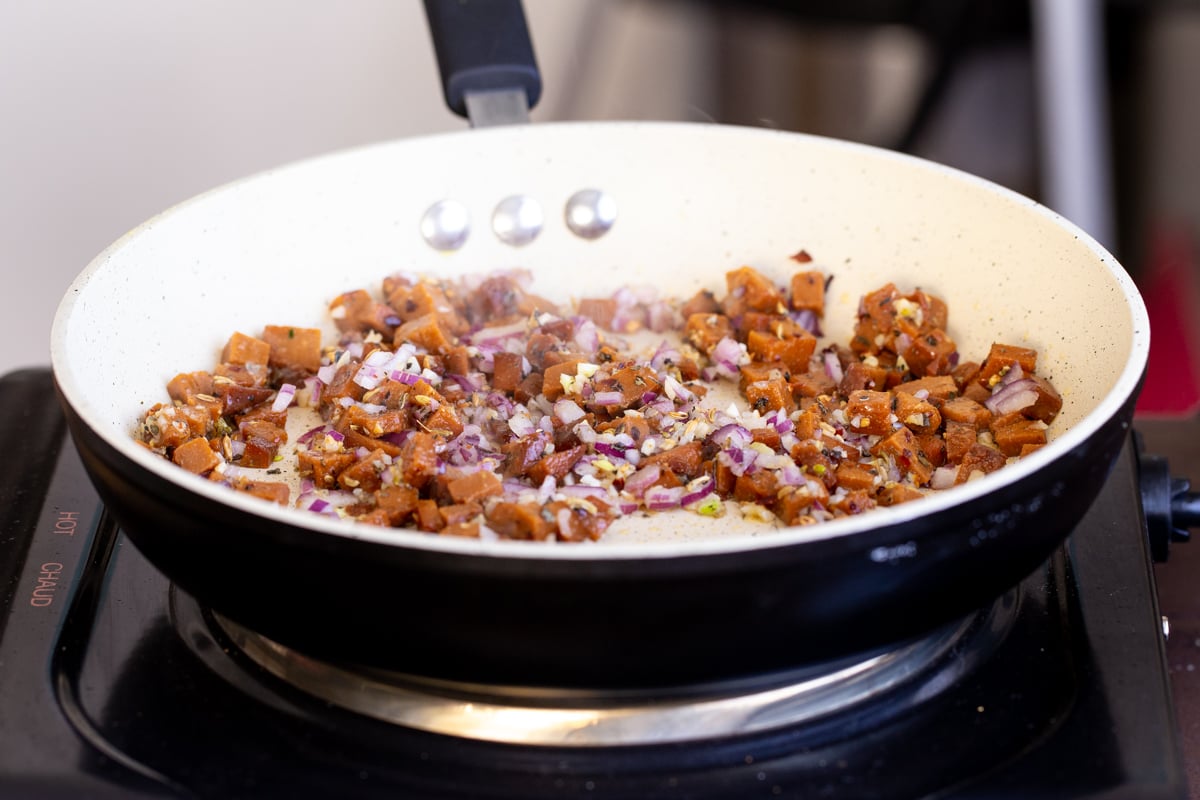 vegan sausage sauteeing in a pan with onion and garlic