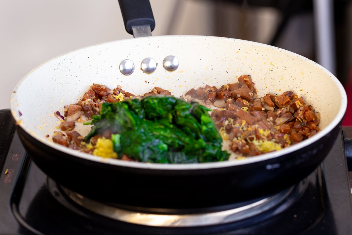 thawed frozen spinach being added to fried sausage in a pan