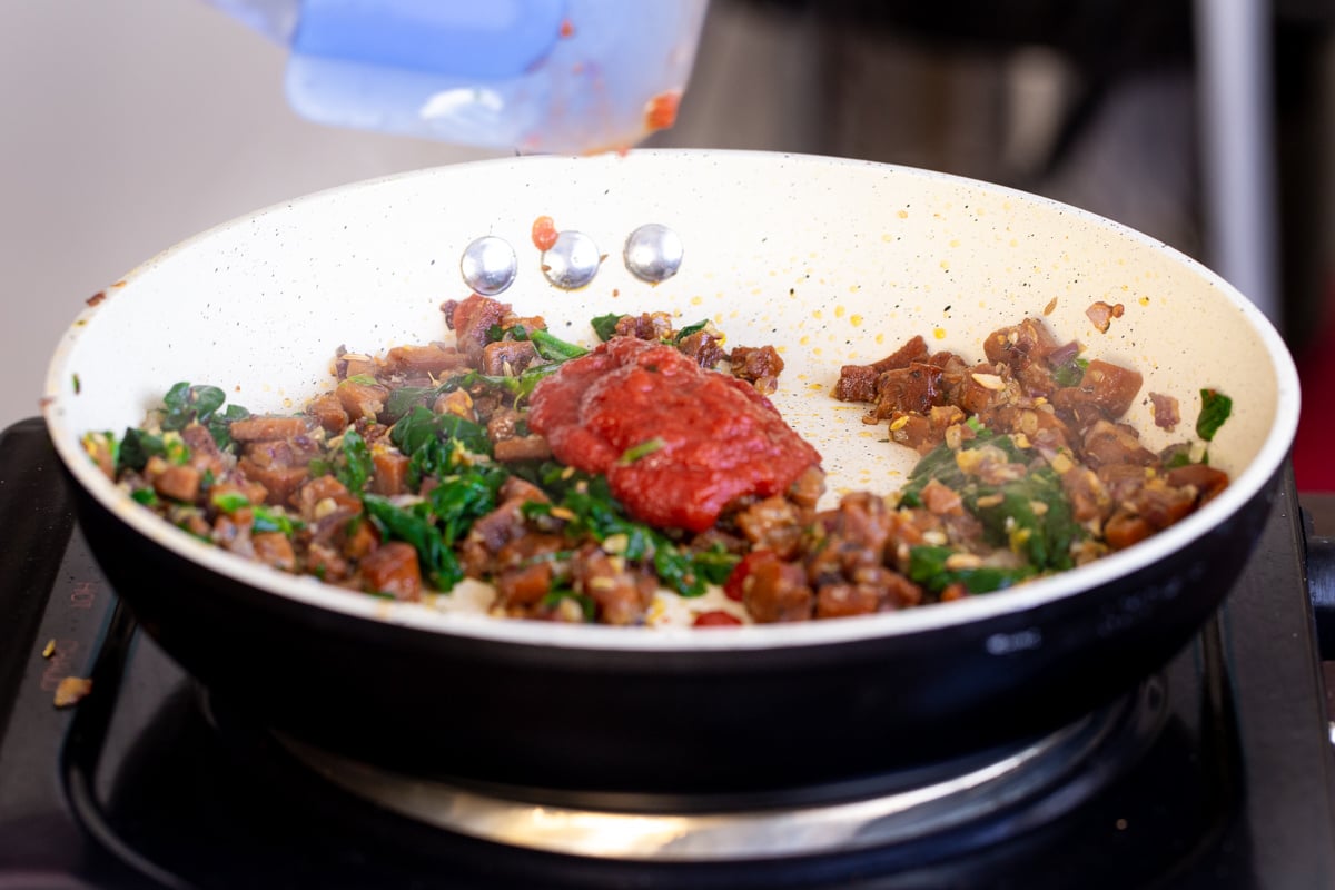 tomato paste, vegan pepperoni and spinach in a sauteeing pan