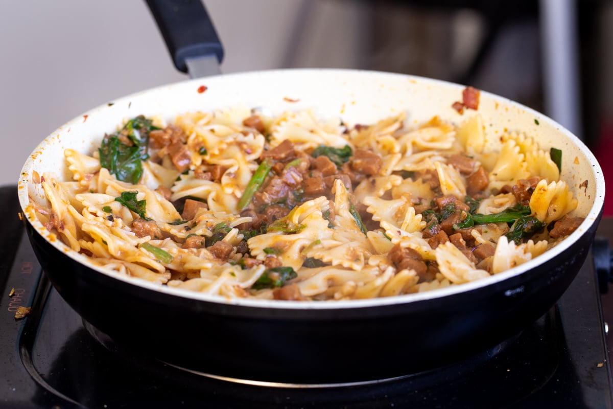 vegan pepperoni pasta being tossed in a white sauteeing pan