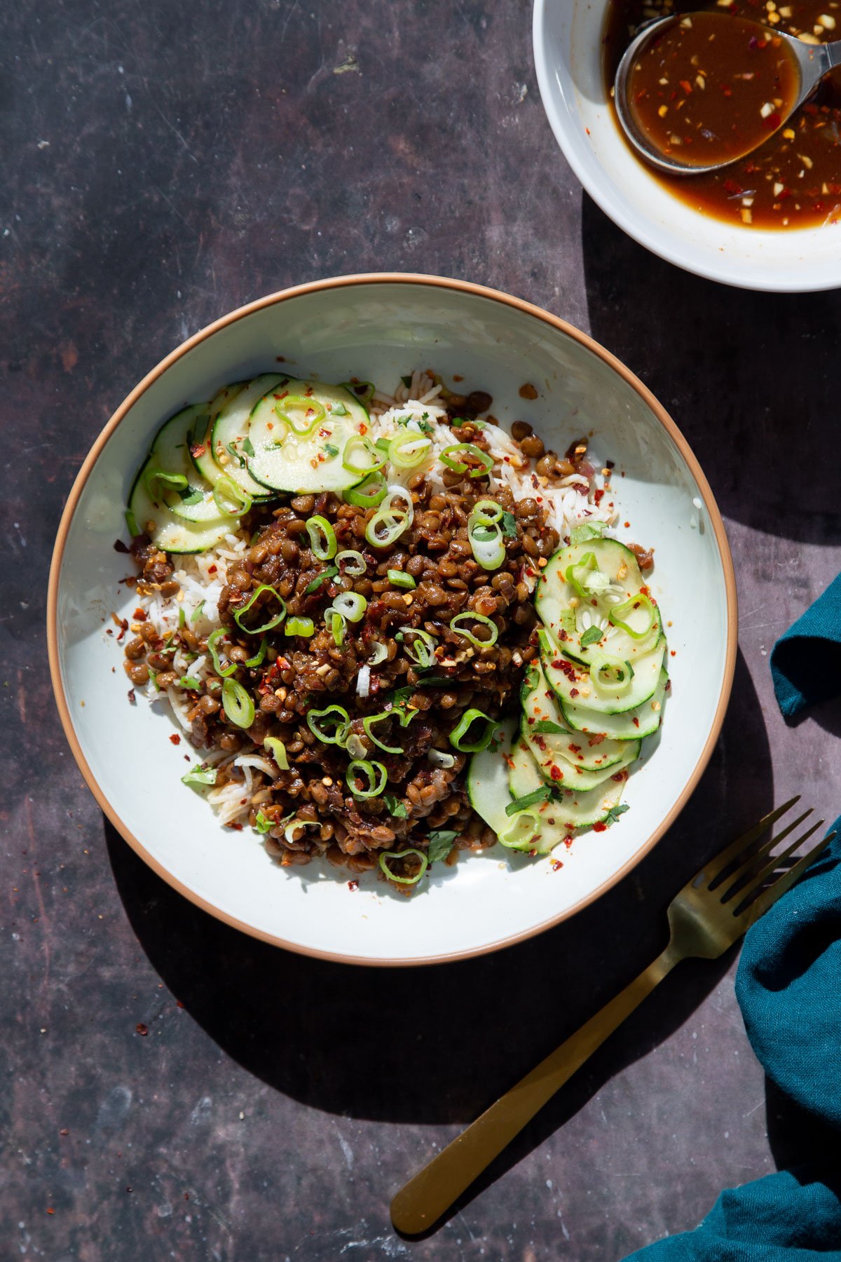 a bowl of vegan caramelized pork lentils served over rice with cucumbers on the side