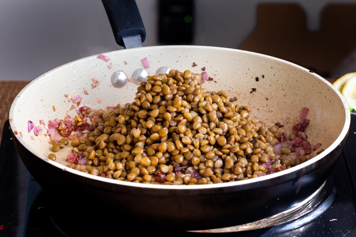 lentils being added to sauteed onions in a pan