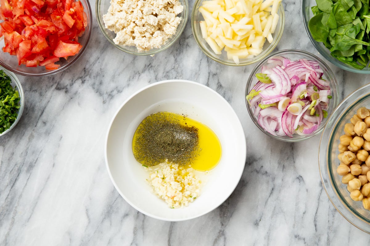 ingredients for lemon dill dressing in a white bowl surrounded by remaining salad ingredients