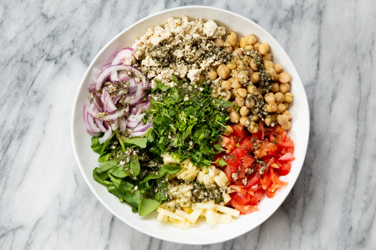 vegan chickpea salad ingredients in a salad bowl with lemon dill dressing drizzled on top