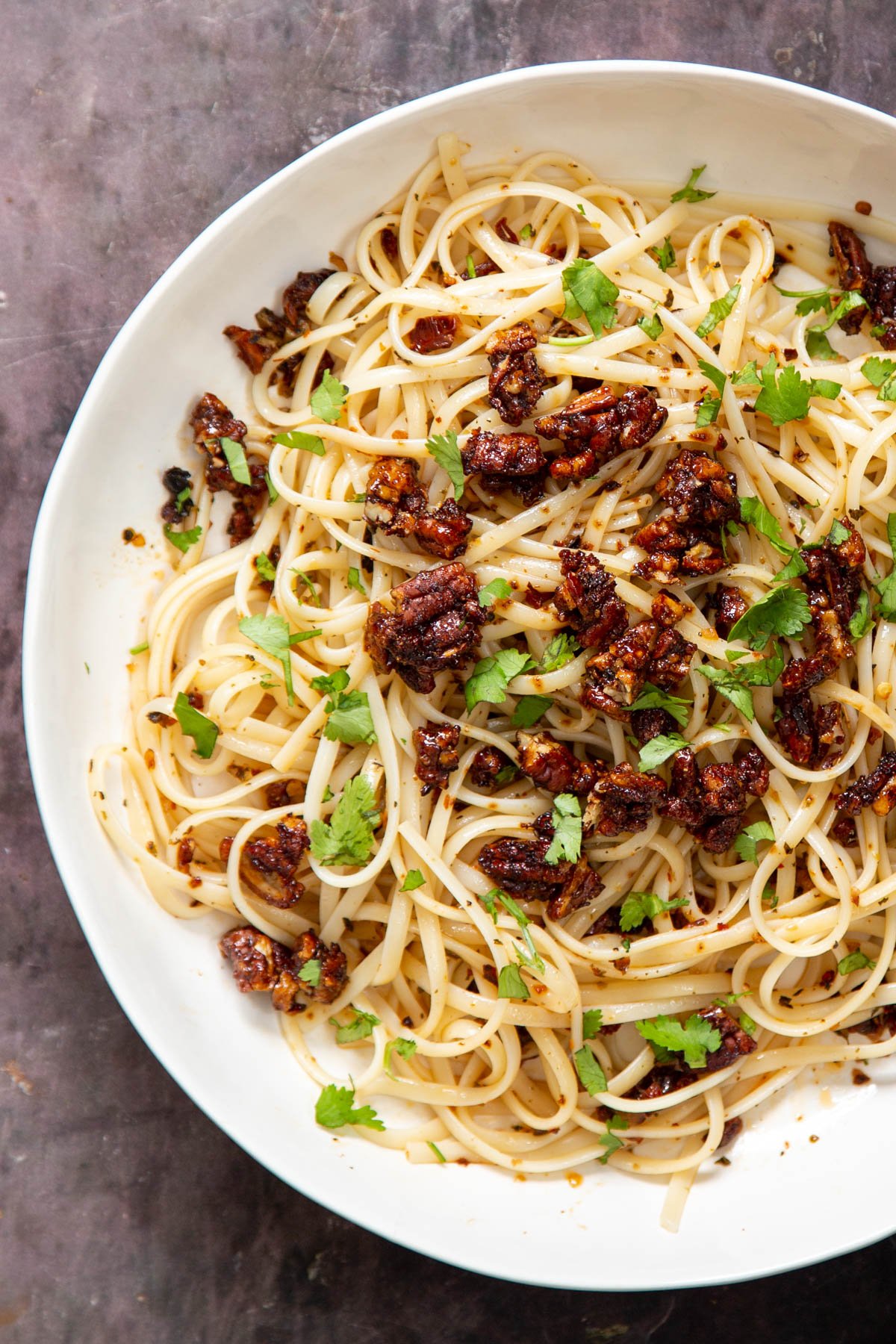 vegan chili garlic oil pasta topped with candied pecans in a white bowl