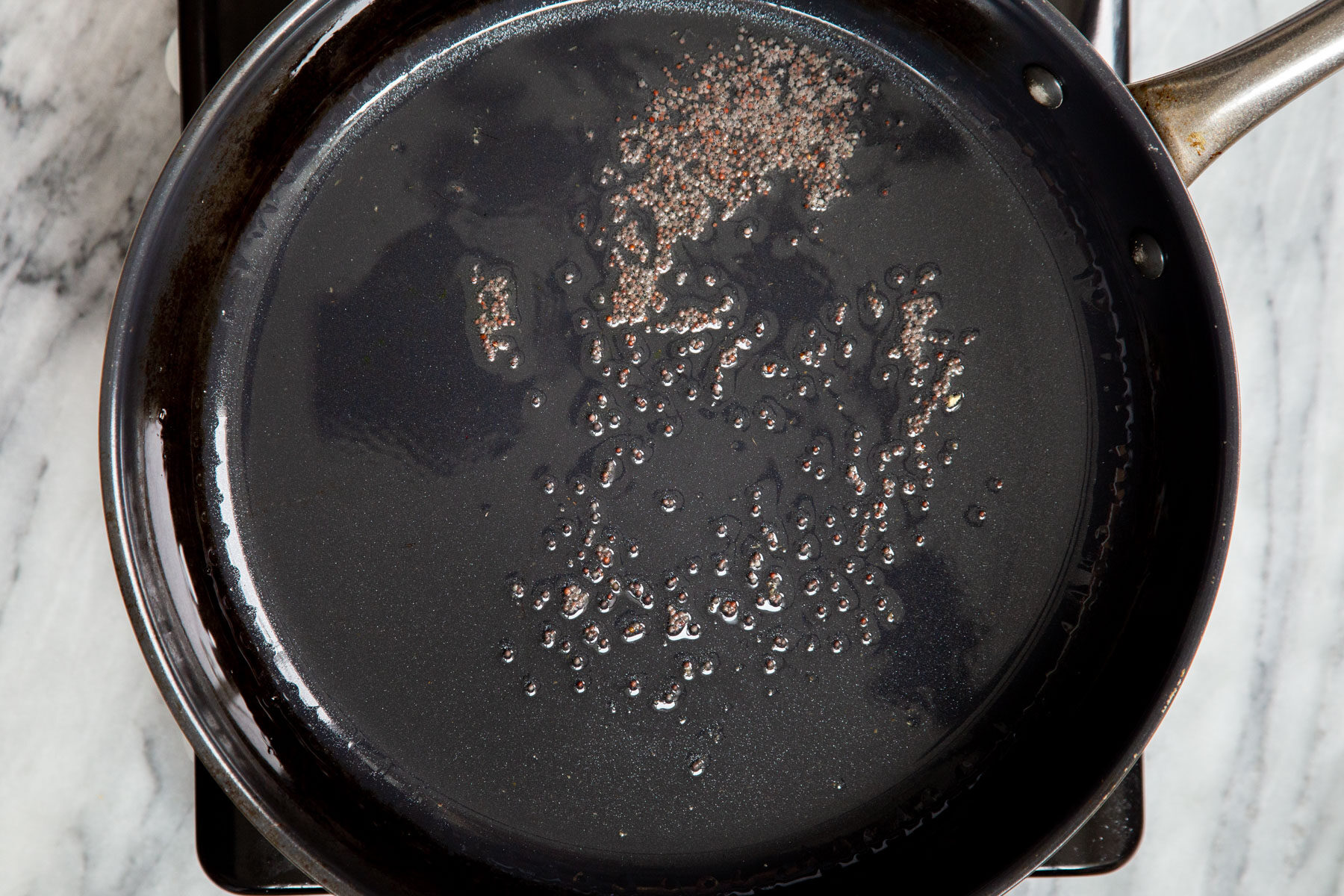 mustard seeds frying in oil in black frying pan 