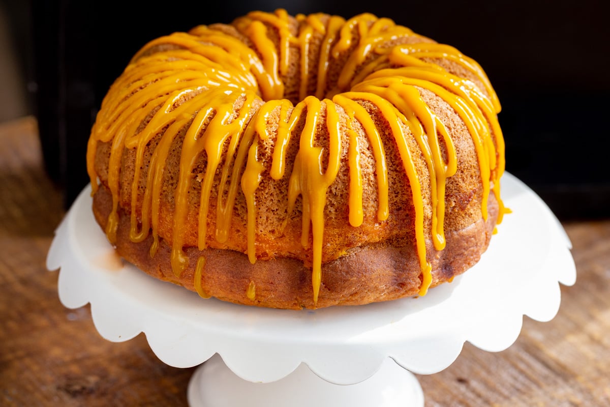 eggless mango bundt cake on a white cake stand with mango drizzle