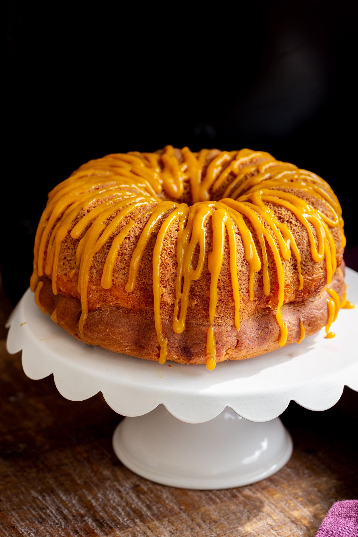 vegan mango bundt cake on a white cake stand drizzled with mango puree