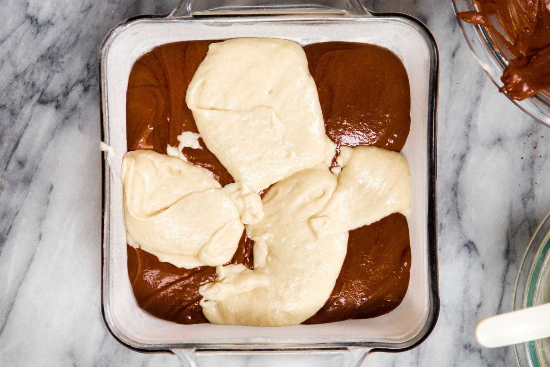 vanilla and chocolate cake batter being added to cake pan to make marble cake recipe