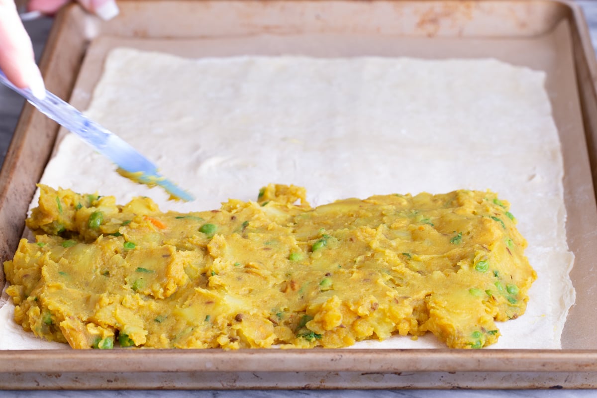 potato filling being spread on puff pastry to make vegan samosa pie