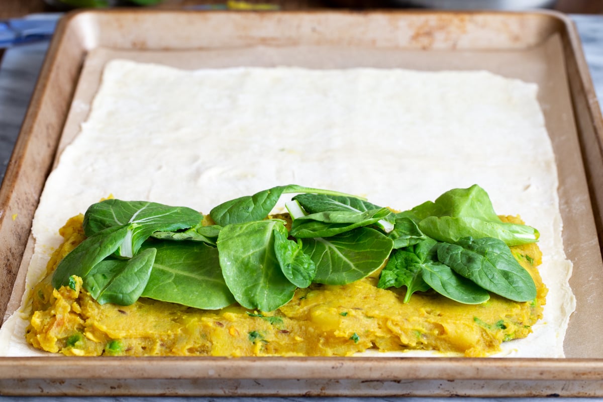 spinach being added as final step of vegan samosa pie assembly