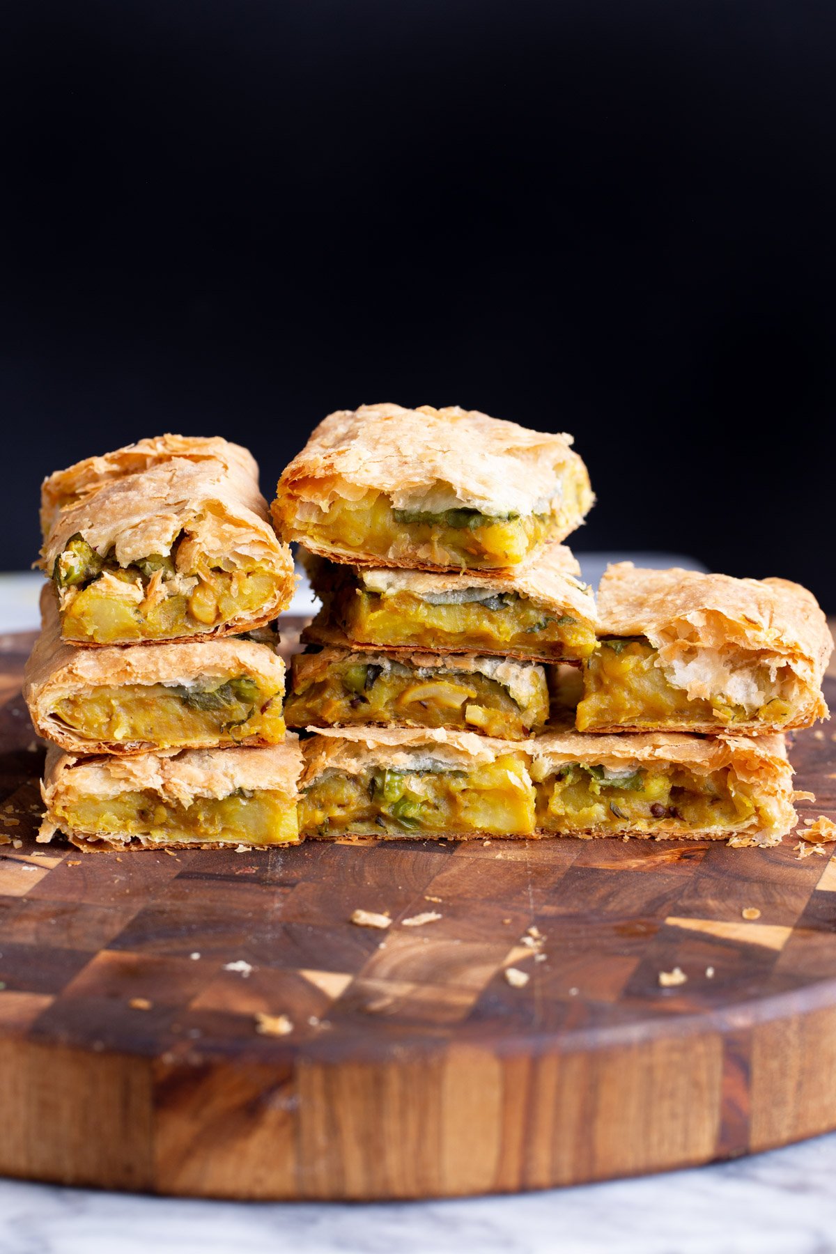 stacked pieces of vegan potato samosa pie on a wooden board