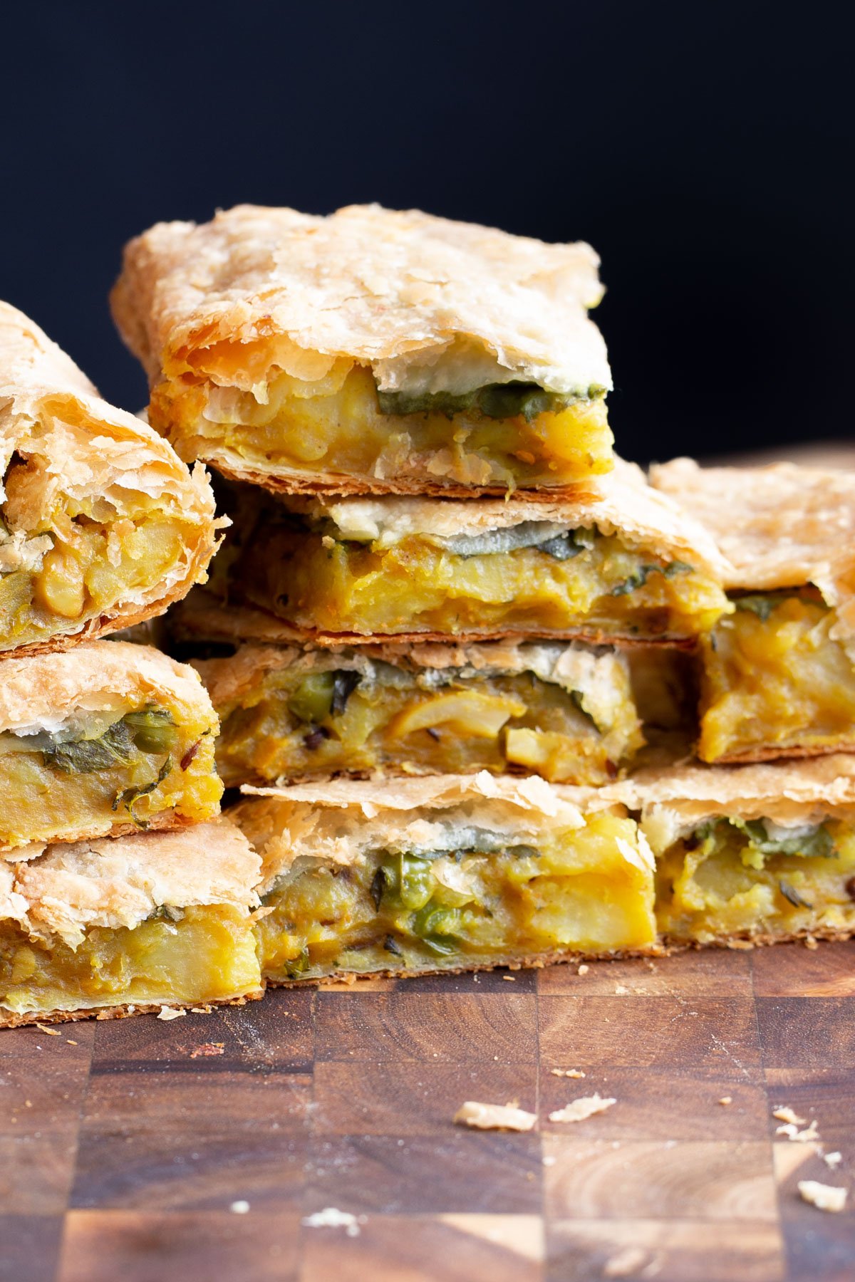 stacked pieces of vegan potato samosa pie on a wooden board