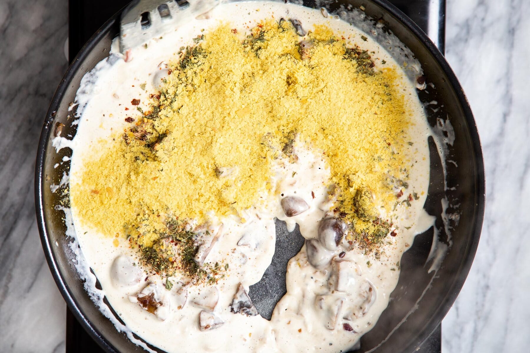 nutritional yeast being added to creamy mushrooms sauce