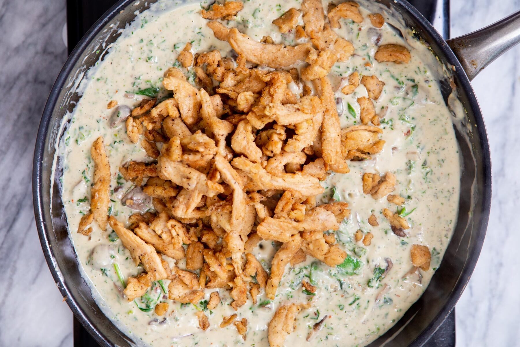 fried soycurls being added to pan with creamy florentine sauce
