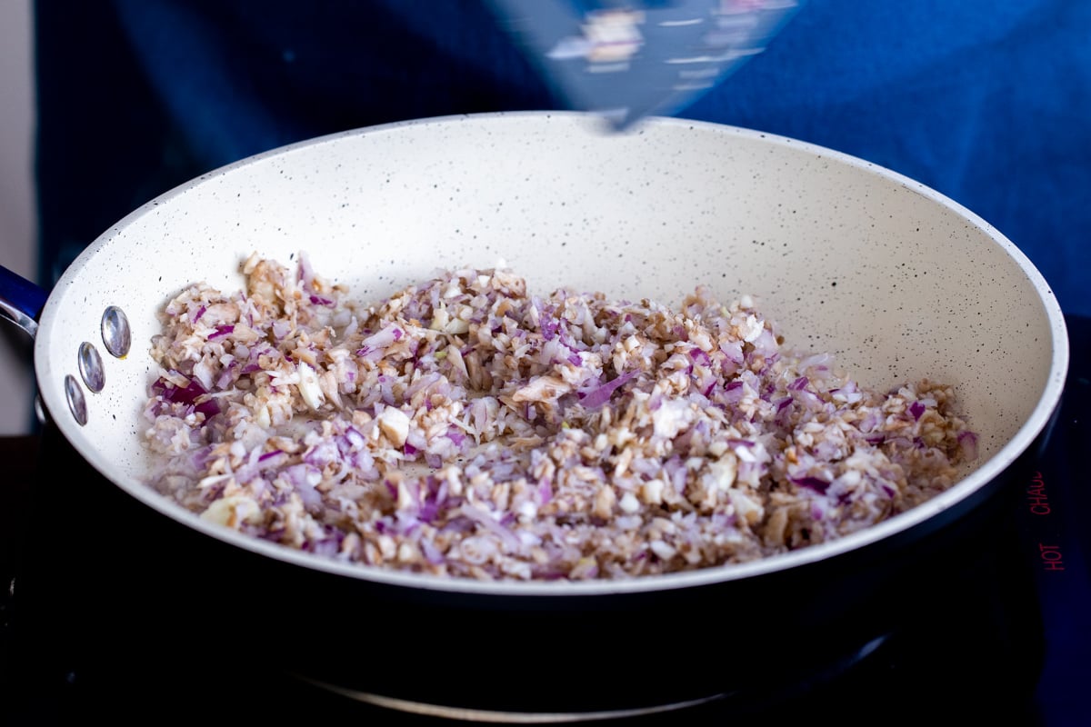 side view of a saucepan with minced mushroom stems and onions