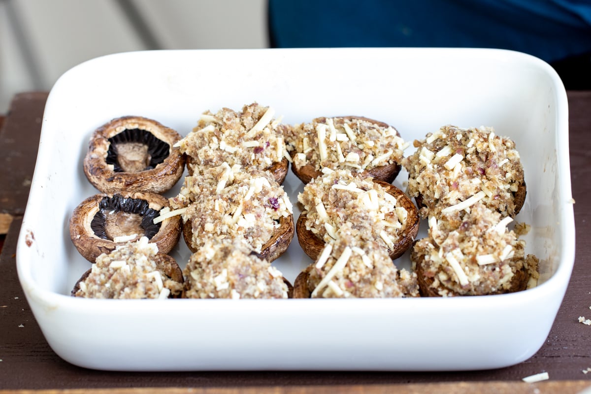 mushroom caps in a white casserole dish being filled with breadcrumbs cheese filling