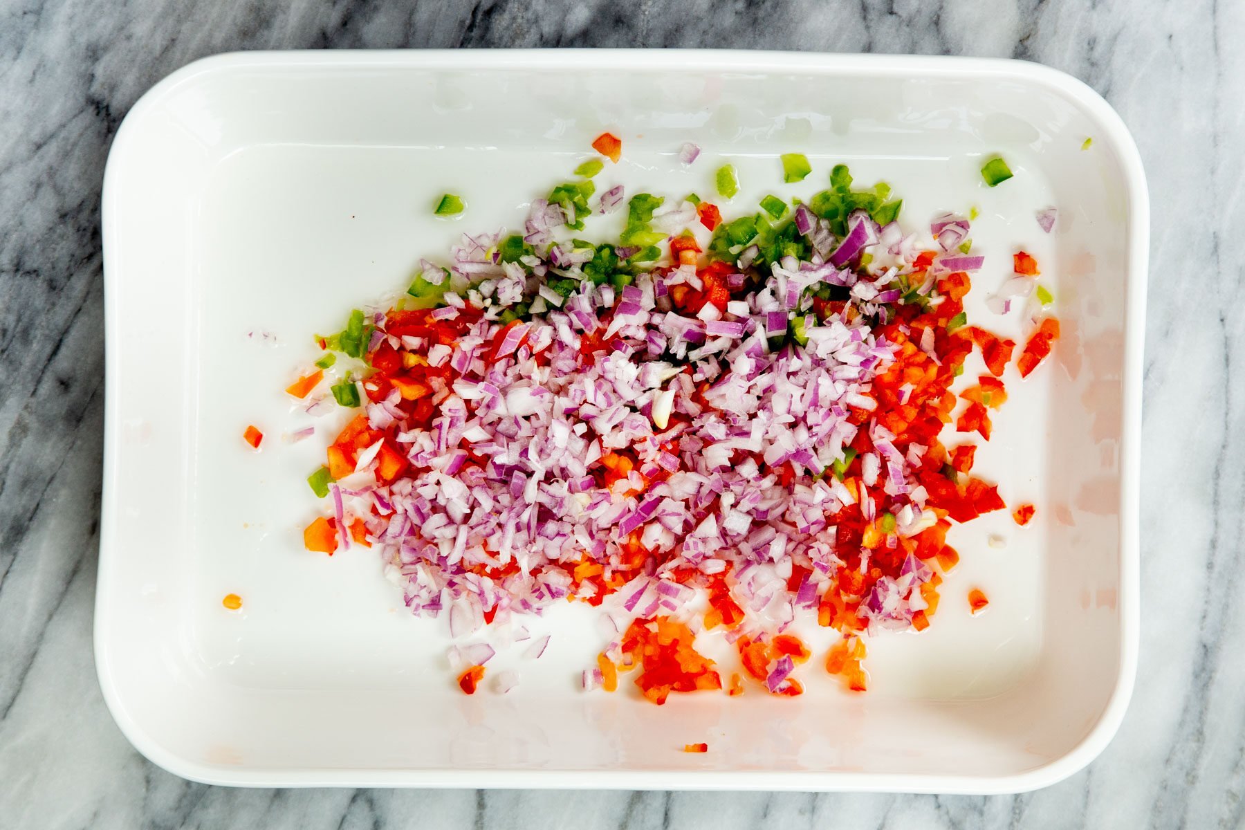 chopped onions and bell pepper in a white casserole dish